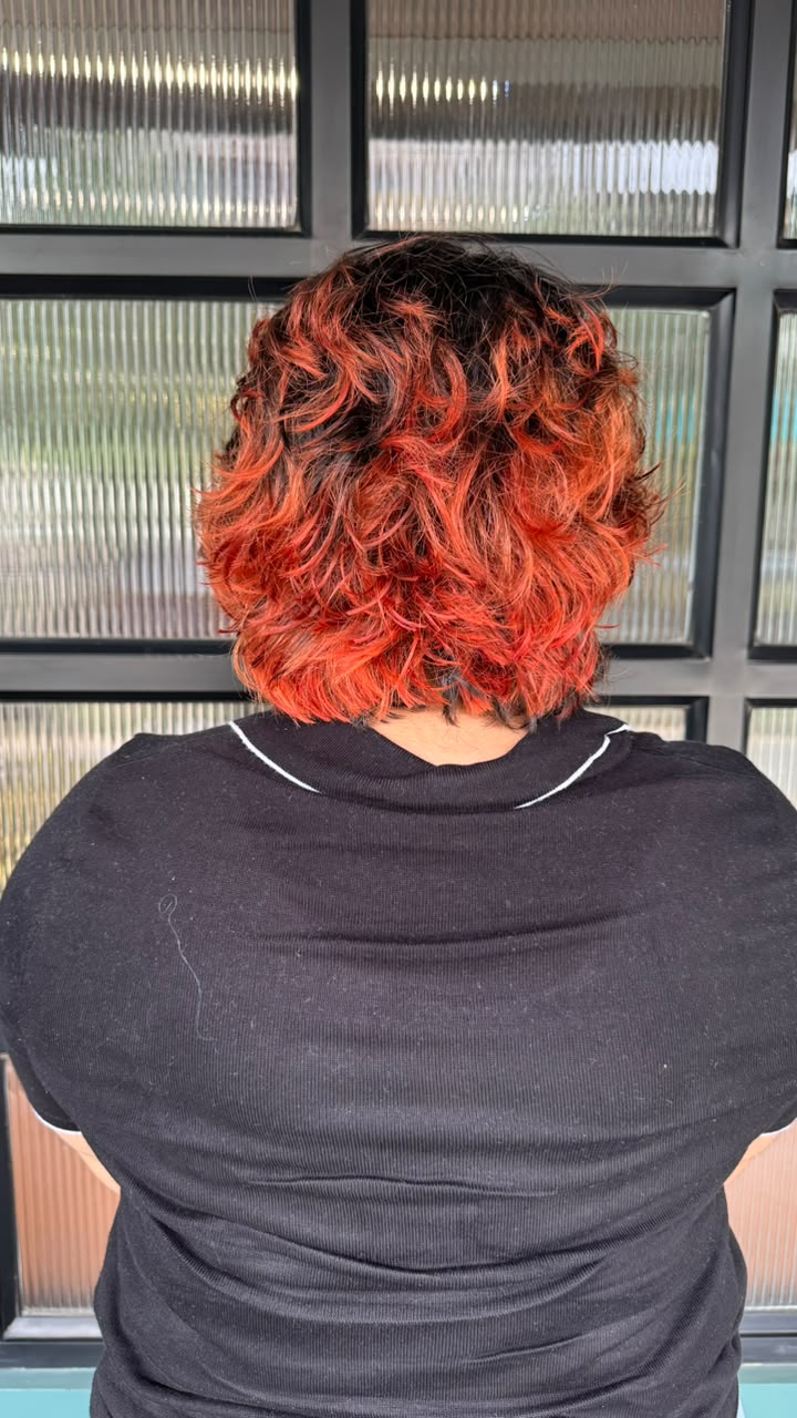 A bold, vibrant red-orange curly hair transformation. The hair is styled in a sh